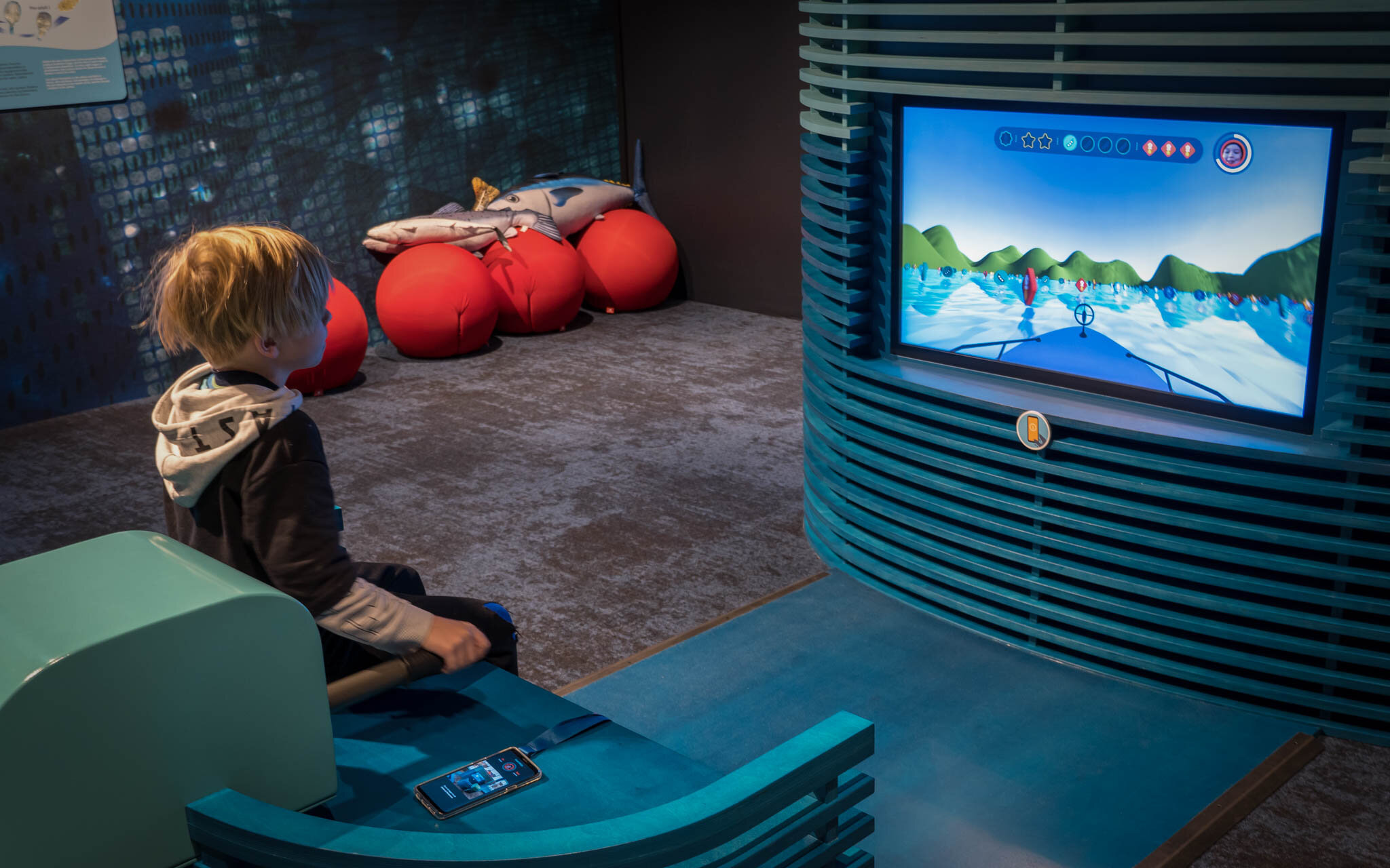 Kid sitting on a pretend motor boat handle looking at a screen with a game view of a boat.