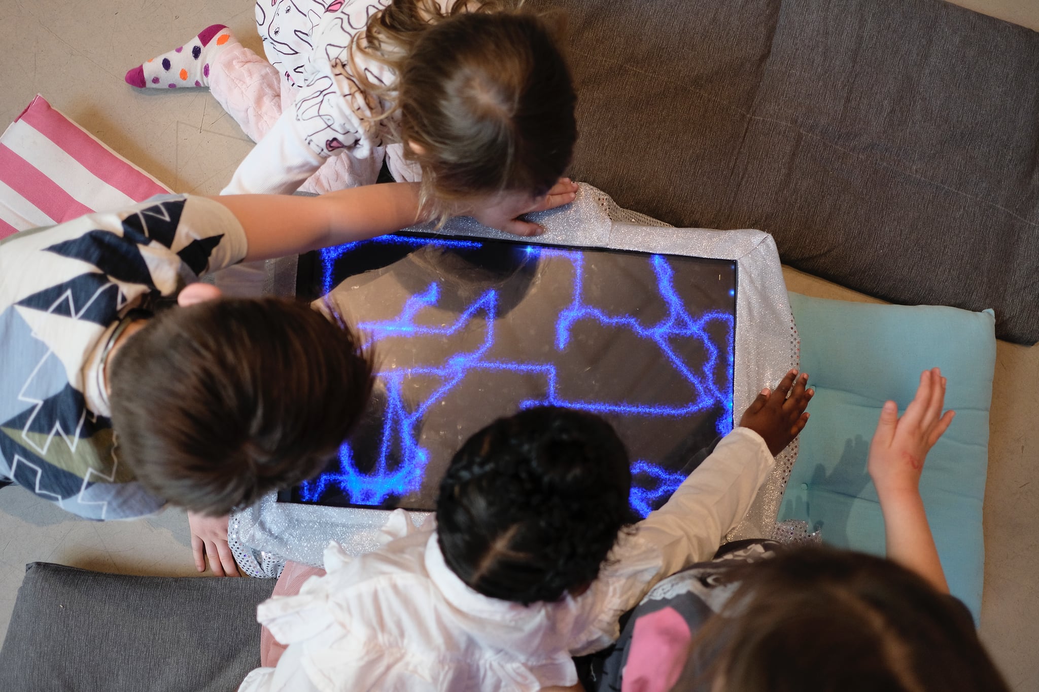 Kids hovering their hands over the edges of a screen displaying drawings from lines of stardust