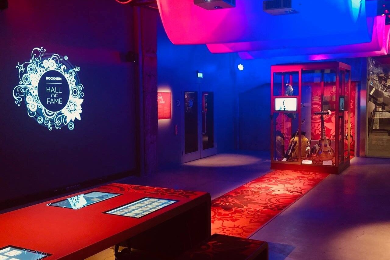 Room lit in strongly lights of strong red, purple and blue with a red carpet that connects into a table with touch screens on it.